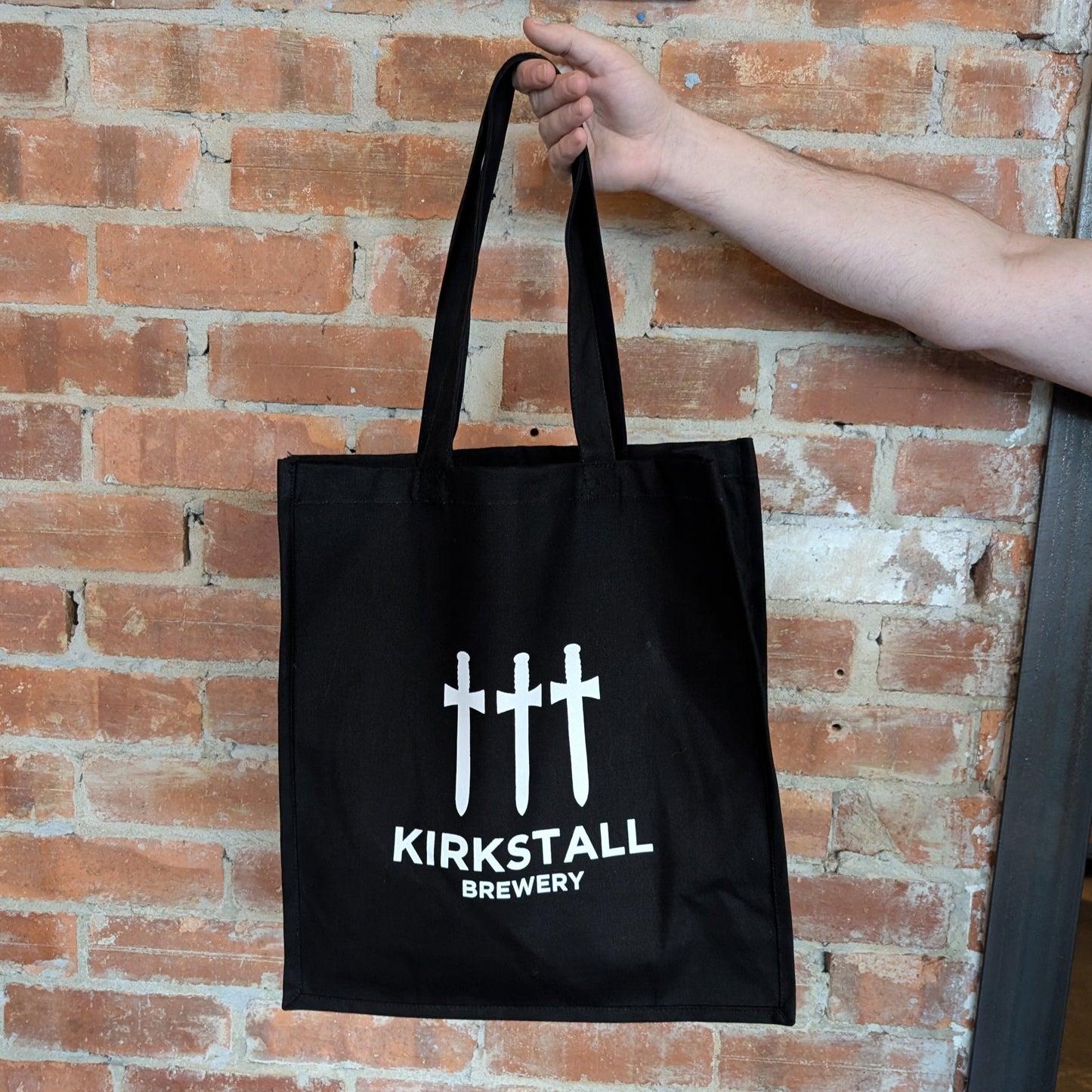 Hand Holding Heavy Duty Three Swords Tote Bag In Front Of Brick Wall